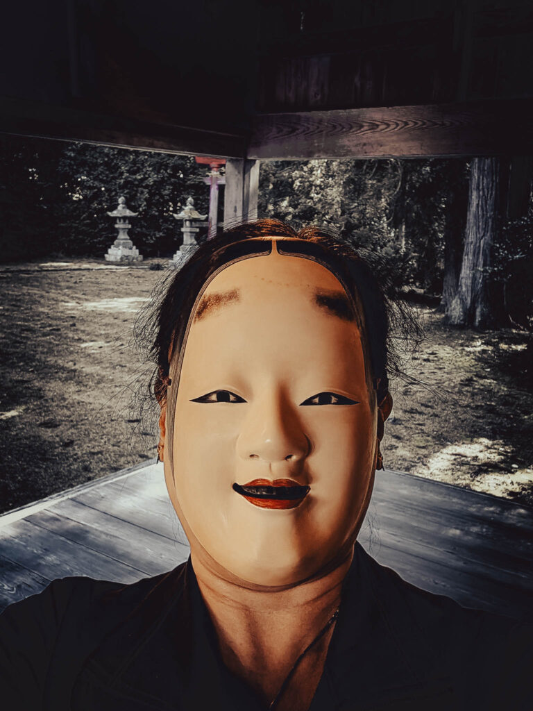 Sado Daizen Shrine Noh Stage, Takeda, Sado Island, rebuilt 1846 (Nov. 6, 2025): KY wearing antique 万媚 (Manbi, demon disguised as a young woman) nō-men, self-photo by KW, photo processing by LW.