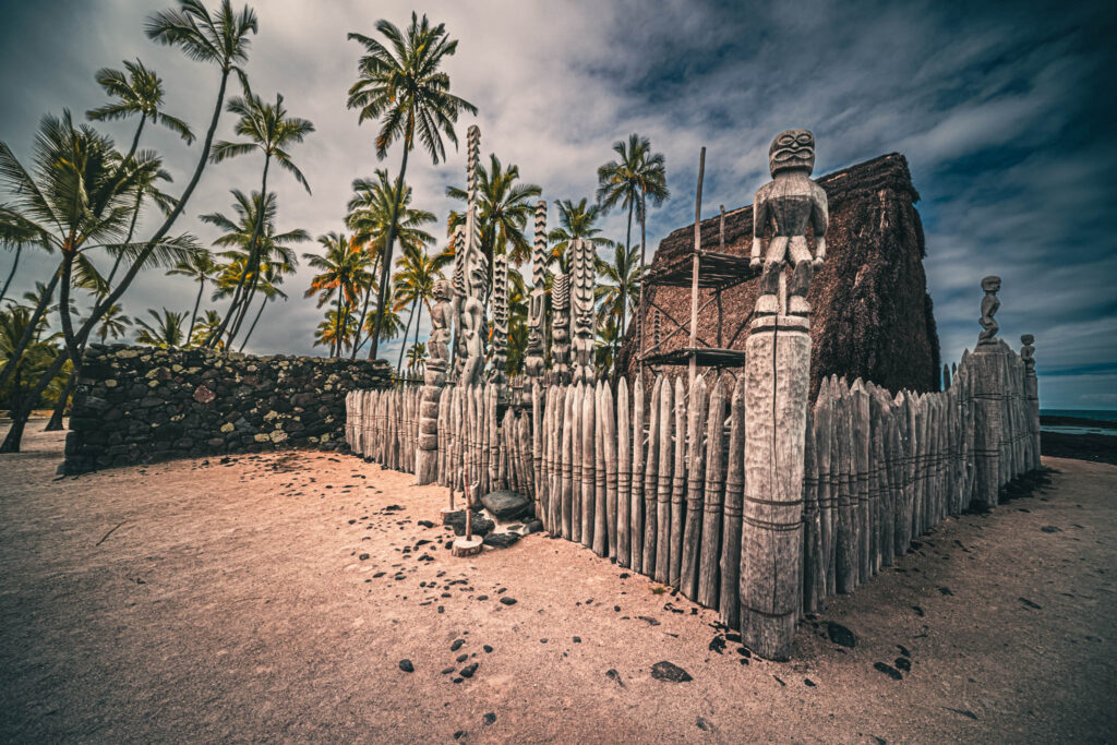 Puʻuhonua o Hōnaunau National Historical Park, Hōnaunau, Hawai'i (photo August 21, 2021): Hale o Keawe (mortuary temple built by or for ruler Keawe-i-kekahi-aliʻi-o-ka-moku c.1700, last restored 2004) with recreated ki'i (divinity statues) and portion of Pā Puʻuhonua (Great Wall of the Place of Refuge originally b. 15th C.).