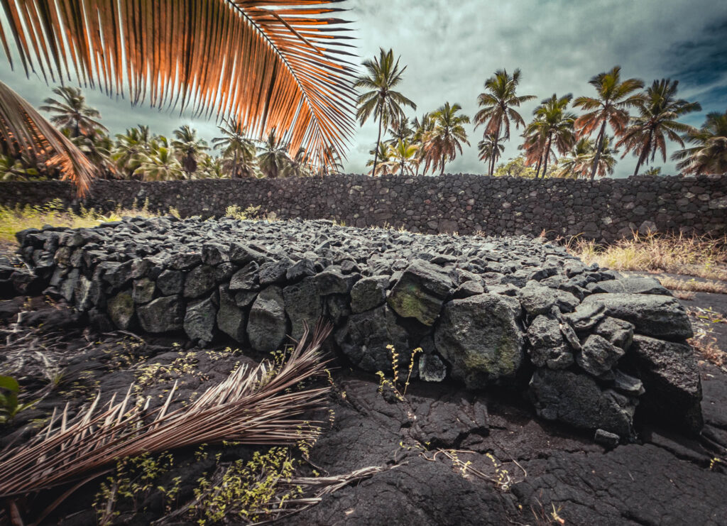 Puʻuhonua o Hōnaunau National Historical Park, Hōnaunau, Hawai'i (photo August 21, 2021): unidentified basalt platform for a structure, with Pā Puʻuhonua (Great Wall of the Place of Refuge, originally b. 15th C.) in background.