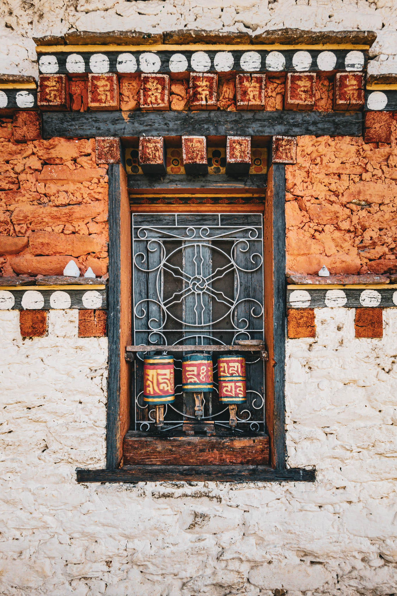Jambay Lhakhang, Bumthang Valley, Bhutan, orig. 659 AD (photo Oct. 26, 2018) exterior window with "'khor lo" prayer wheels against "kemar" painted orange-red frieze.