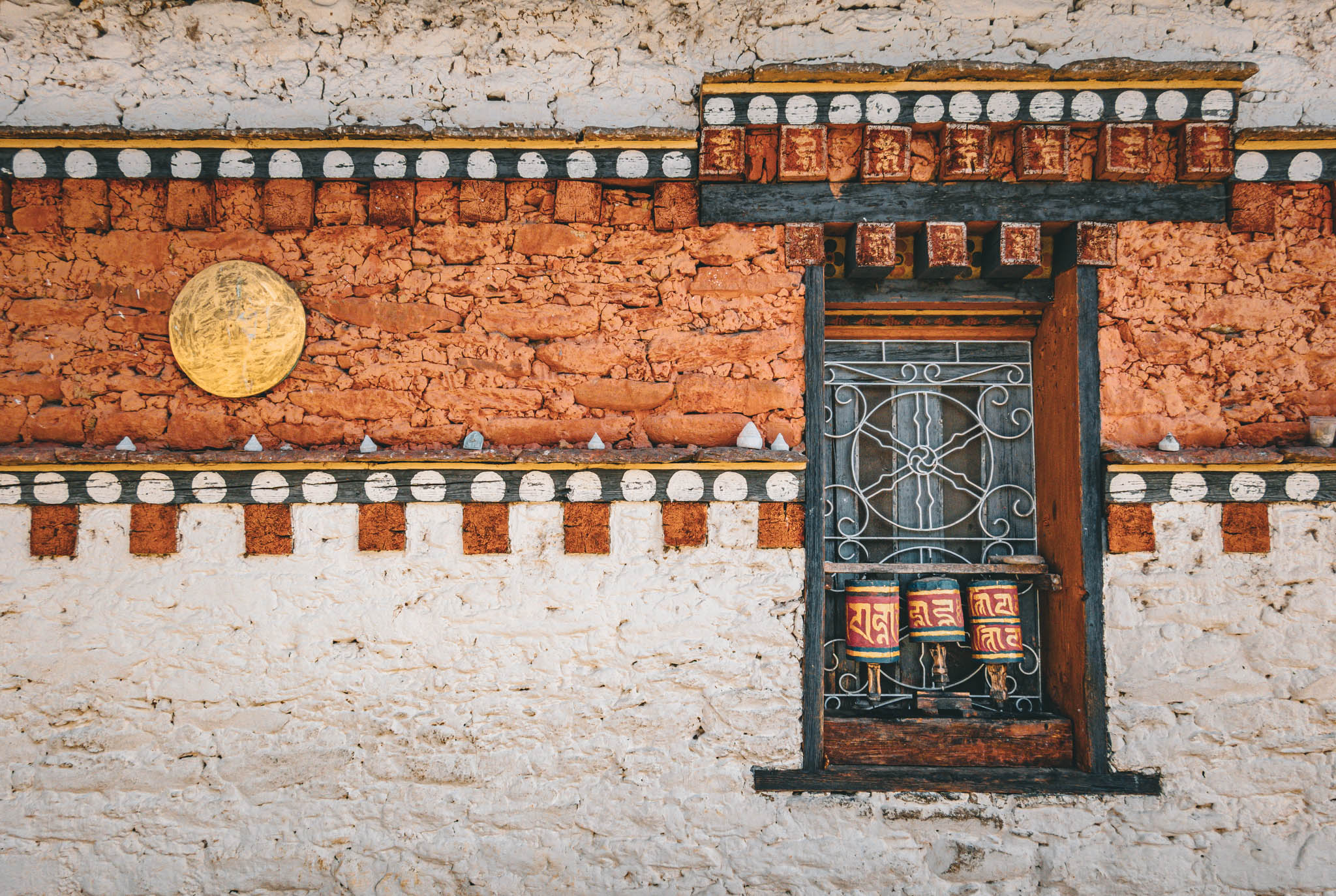 Jambay Lhakhang, Bumthang Valley, Bhutan, orig. 659 AD (photo Oct. 26, 2018) exterior window with "'khor lo" prayer wheels against "kemar" painted orange-red frieze.