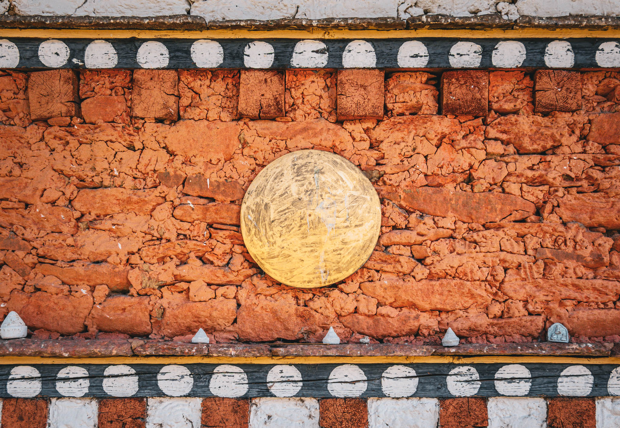 Jambay Lhakhang, Bumthang Valley, Bhutan, orig. 659 AD (photo Oct. 26, 2018) exterior wall detail of "kemar" painted orange-red frieze with applied solar disk.