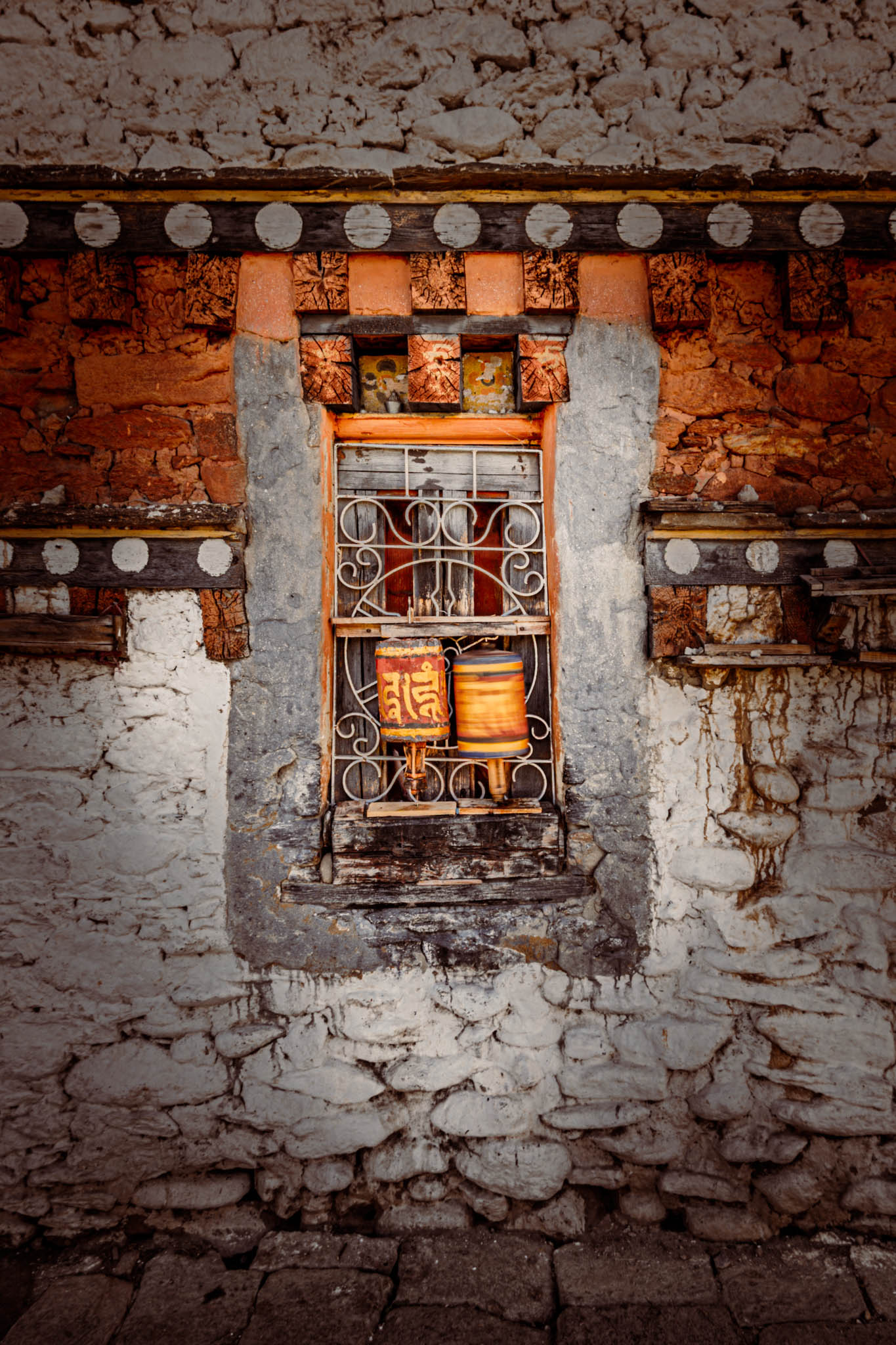 Jambay Lhakhang, Bumthang Valley, Bhutan, orig. 659 AD (photo Oct. 26, 2018) exterior window with "'khor lo" prayer wheels against "kemar" painted orange-red frieze.