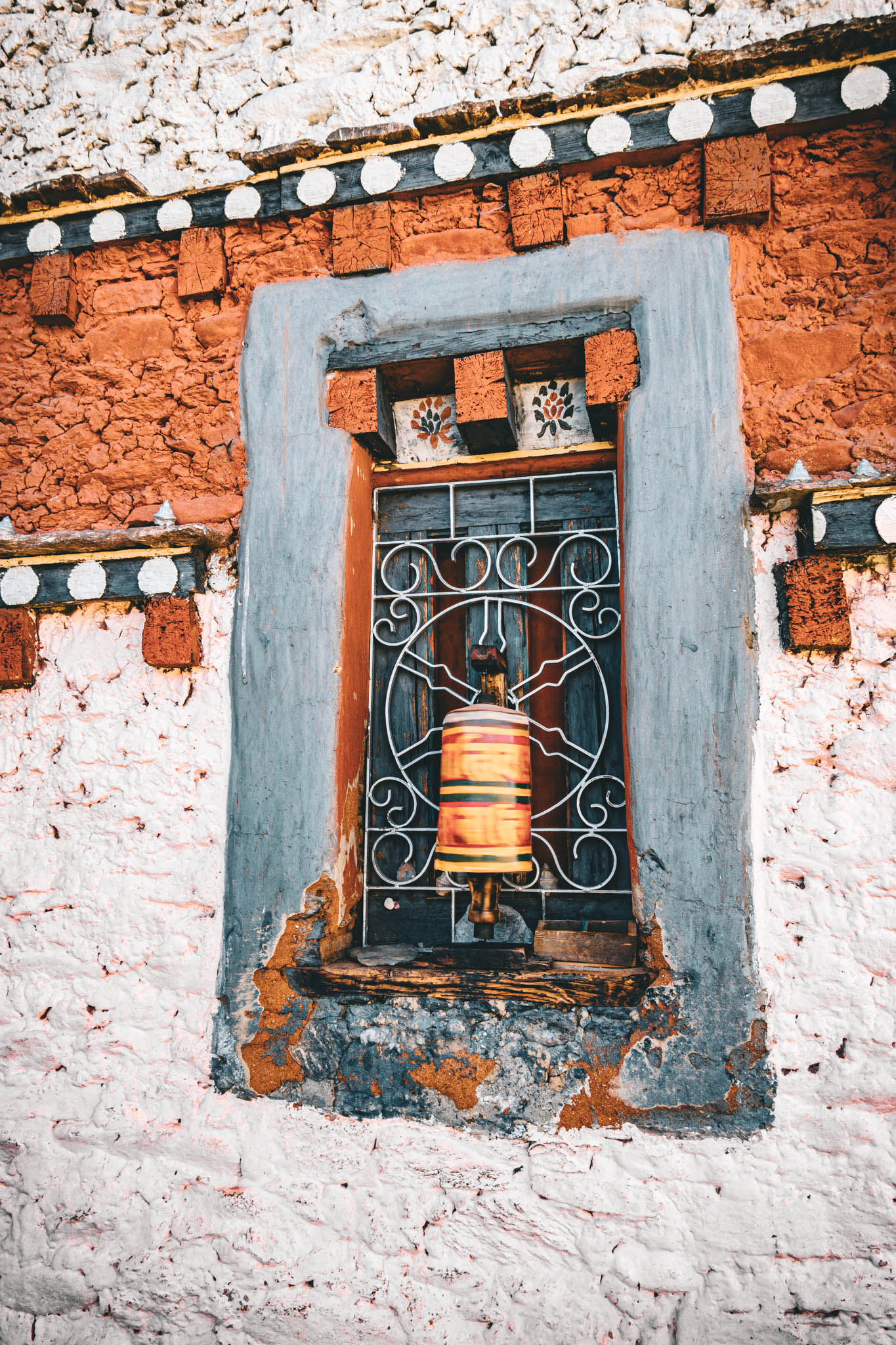 Jambay Lhakhang, Bumthang Valley, Bhutan, orig. 659 AD (photo Oct. 26, 2018) exterior window with "'khor lo" prayer wheel against "kemar" painted orange-red frieze.