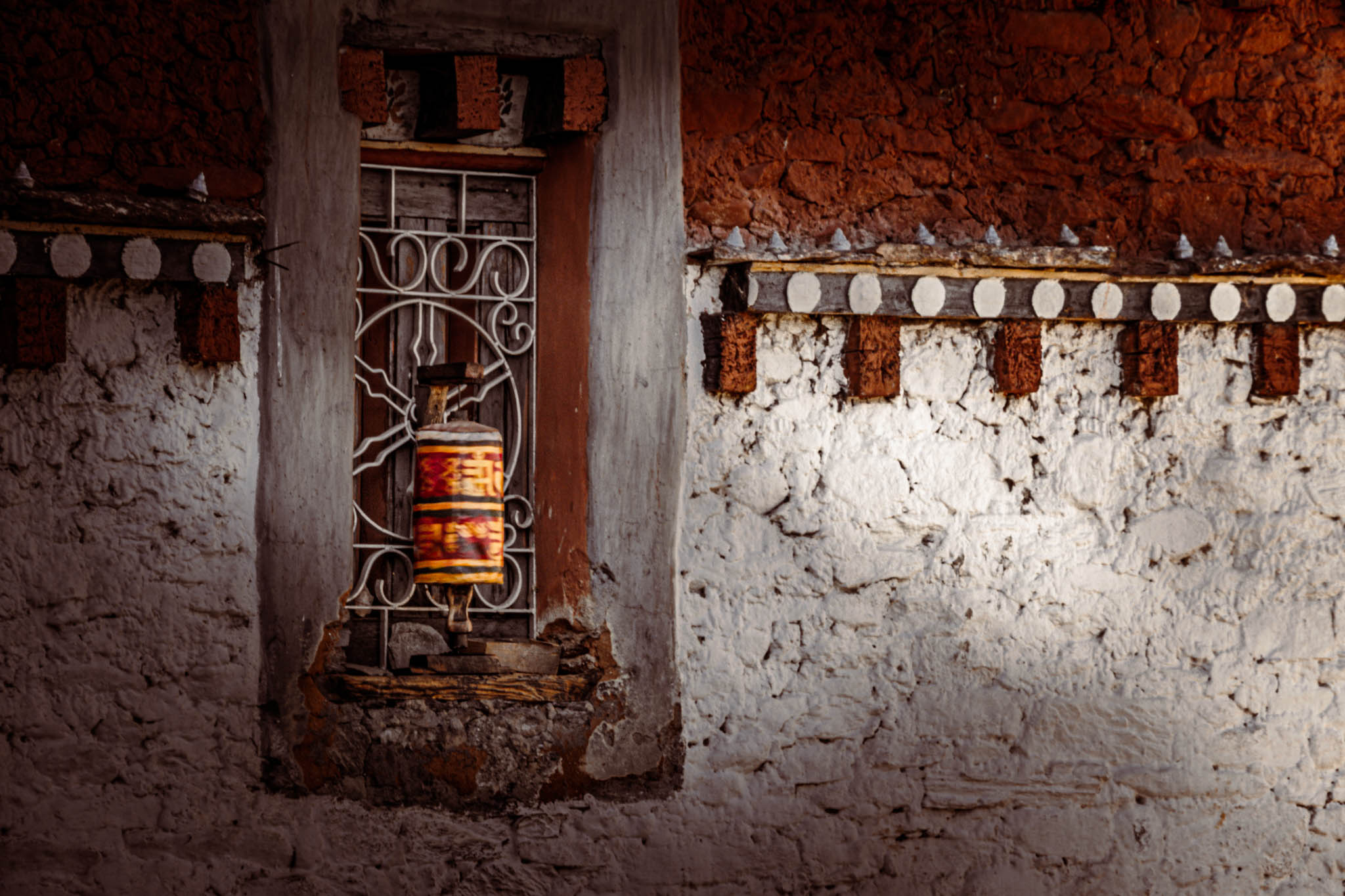 Jambay Lhakhang, Bumthang Valley, Bhutan, orig. 659 AD (photo Oct. 26, 2018) exterior window with "'khor lo" prayer wheels against "kemar" painted orange-red frieze.