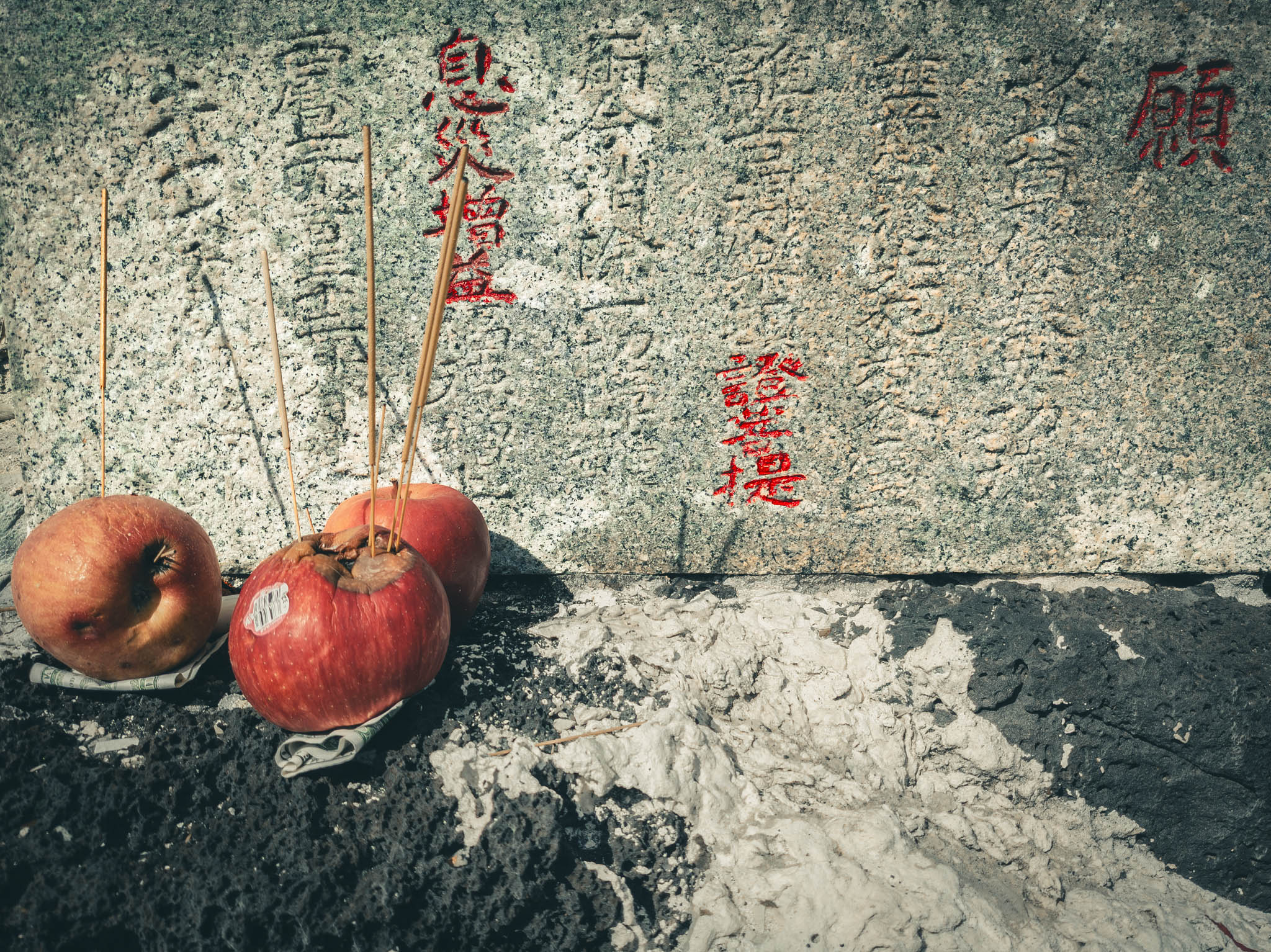 Japanese Fishing Shrine, Kalanianaʻole Highway, Oahu Island (photo 15 August 2021): incense, fruit, and money offerings at base of Jizo sculpture, inscription partially filled with red pigment.